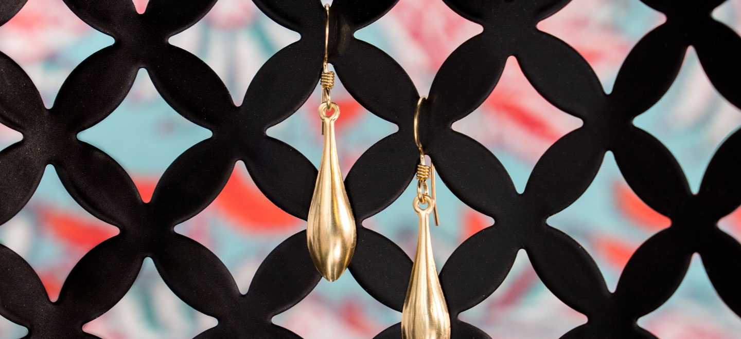 Pair of gold teardrop dangle earrings hanging from black geometric display