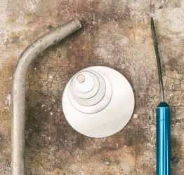 Stack of sterling silver round blanks next to jewelry soldering torch and pick