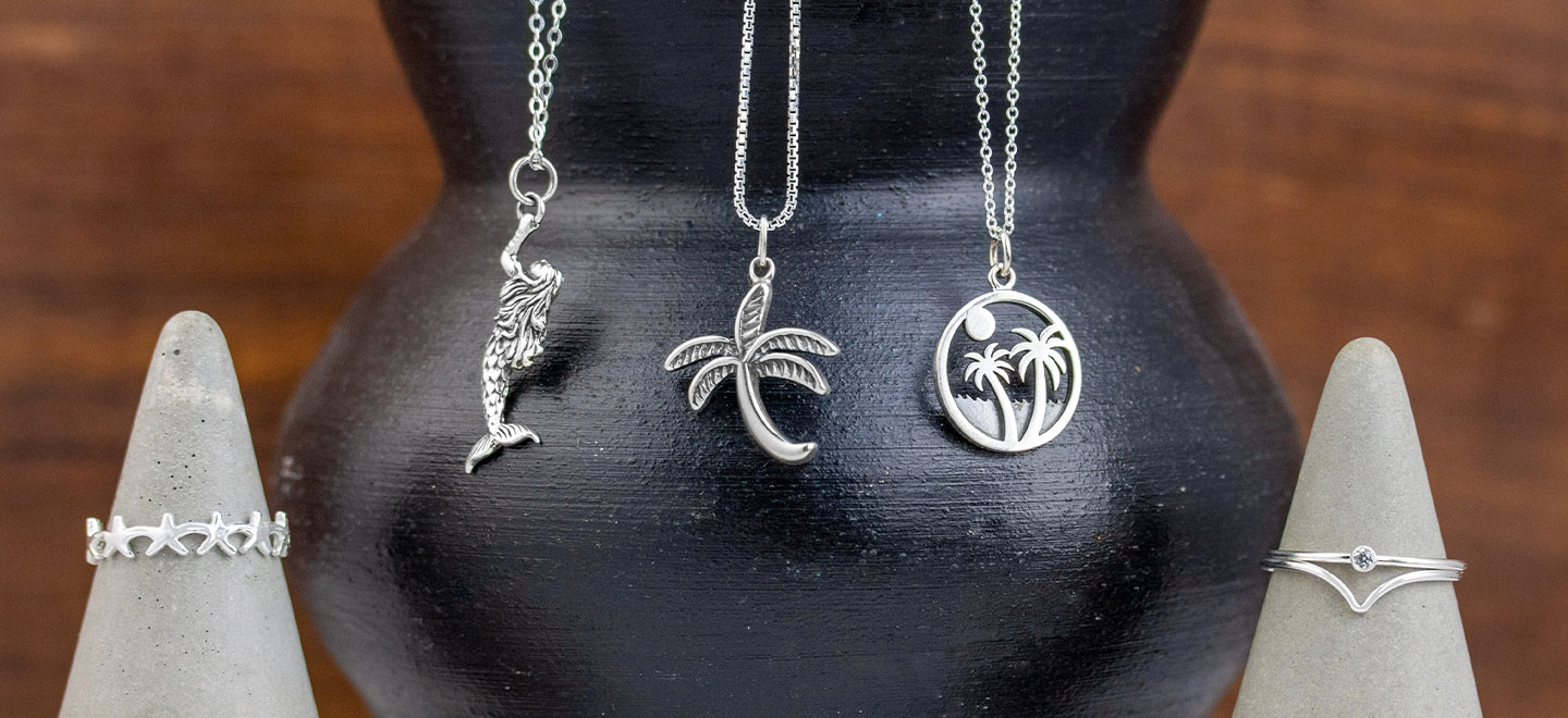 Sterling silver necklaces draped on a black vase with two cement ring holders displaying sterling rings