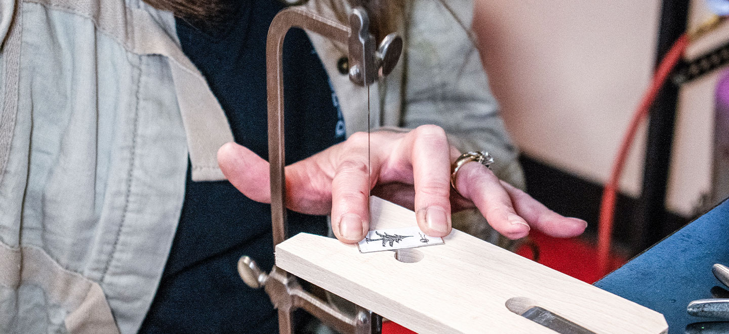 Jeweler using saw to cut and pierce a piece of sterling silver sheet