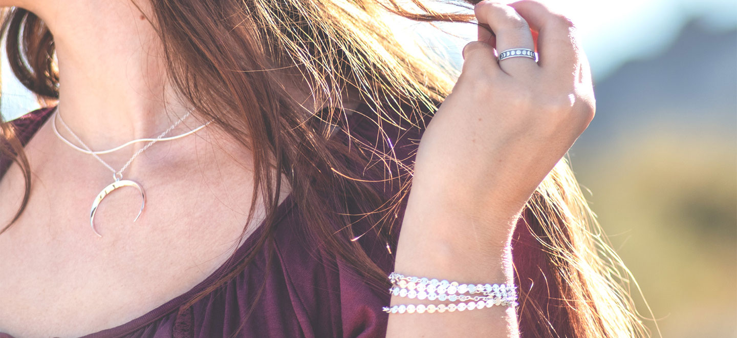 Women's neckline showcasing a sterling silver necklace and hand holding hair with ring and bracelet on